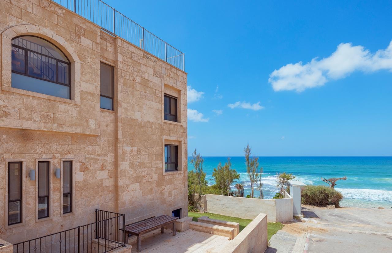 Full stone facade of the villa with rooftop terrace and sea beyond